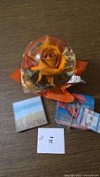 Orange rose encased in clear globe alongside wrapped stack of six coastal coasters