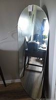 Full view of tall frameless oval mirror leaning against wall