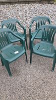 Four green plastic patio chairs arranged outdoors showing style and condition
