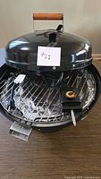 Overall view of black tabletop electric grill with lid open showing grate, heating element, control knob and power cord