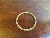 Full view of twisted gold-tone bangle bracelet on wood surface