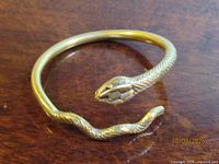 Full view of gold-tone snake bracelet on wood surface