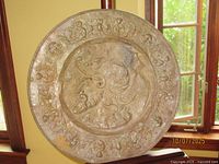 Full view of circular embossed copper plaque on stand