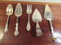 All five silver plated serving utensils on wood surface