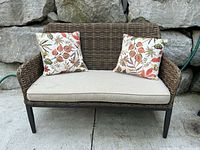 Front view of resin wicker loveseat with cushion and pillows