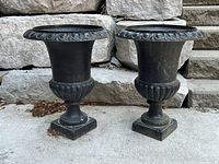 pair of black cast iron urn planters on outdoor surface