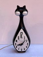 Full front view of black cat clock with dial and cord visible