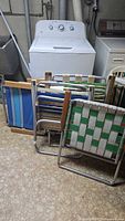Folded chairs and beach chairs stacked against washing machine