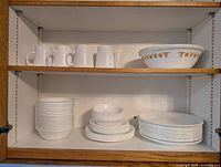 Cabinet shelves with white Corelle mugs, stacked bowls and plates