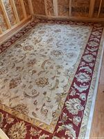 Full view of rectangular beige and cranberry red bordered floral area rug
