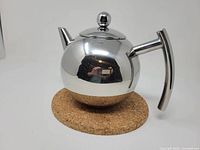 Front view of spherical stainless steel teapot showing spout, handle, lid