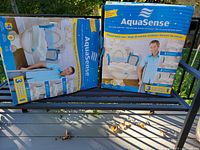 Two boxed AquaSense raised toilet seats on bench