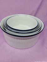 Three nested Dansk white souffle dishes showing ribbed sides and blue rim