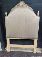 Front view of one headboard showing upholstery, crest, finials, legs