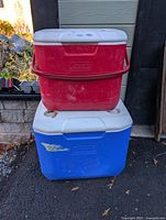 Front view of red cooler stacked on blue wheeled cooler