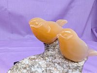 Close view of two orange selenite birds on marble base