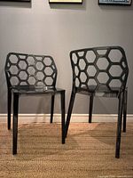 Front angled view of both smoked lucite chairs showing honeycomb backs and overall shape