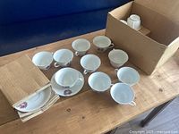 Overview of teacups and saucers with packing materials and box