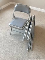 Three gray metal folding chairs, one open two folded