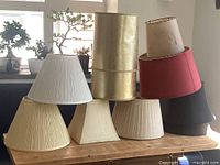 Group shot showing ten assorted lamp shades stacked on wooden surface