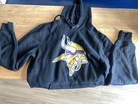 Front view of black Vikings hoodie laid flat showing logo and sleeves