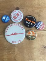 Group shot of all six pinback buttons arranged on wood surface