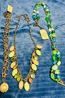 All three necklaces laid on blue fabric showing overall designs and attached tags