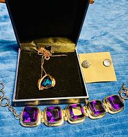 Overview of necklace in box, earrings on card, and purple stone bracelet