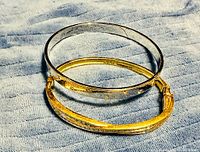 Gold-tone pavé crystal bangle and silver-tone crystal station bangle on fabric background