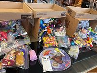 Overall lot showing boxes and bags filled with assorted small toys, raccoon pad in foreground