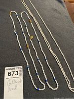 Three pearl necklaces laid out on cloth showing bead details and clasps with lot tag