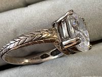 Profile view of silver ring showing engraved band and prong-set clear gemstone