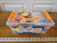 Closed clear box with orange handle and latches, ruler for scale