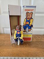 Toy bear on unicycle beside opened box front view