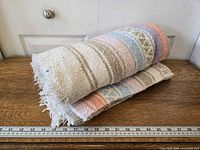 Rolled pastel striped Mexican blanket on wooden surface with ruler for scale