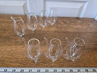 Seven clear port sipper glasses arranged on wood surface with ruler for scale