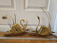 Both brass and wood swan wall hangings side by side with ruler for scale