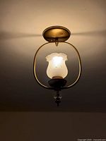 Full view of hanging lantern light mounted on ceiling, showing brass frame and frosted shade