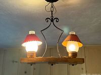 Full view of chandelier lit, showing wood base, two lights, iron scroll hanger, chain