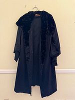 Full frontal view of long black coat with fur collar hanging on hanger