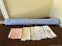 Rolled blue embroidered tablecloth with five folded napkins