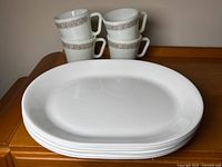 Stack of five white oval Corelle plates with four Pyrex cups behind