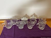 Group shot showing all eight glass creamers and sugars on purple cloth