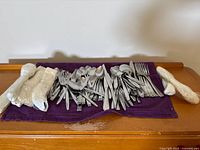 Full lot of stainless flatware spread on purple cloth, bundles at sides