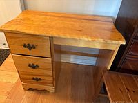 Front view of pine desk showing three drawers and chair partially visible