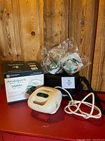 Compressor unit, sealed nebulizer parts, carrying case, box and power cord grouped on table