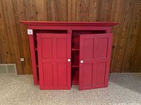 Front view of red wooden cabinet with detached doors and interior shelves visible