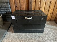 Front view of black steam trunk with metal slats and replacement white handle