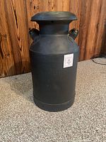 Front view of black milk can showing lid, embossed text, lot tag