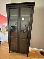 Closed view of tall dark brown-black IKEA Hemnes cabinet with glass doors